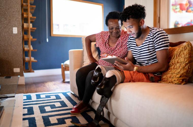 Black woman and a disabled black man sitting on a sofa using an ipad 