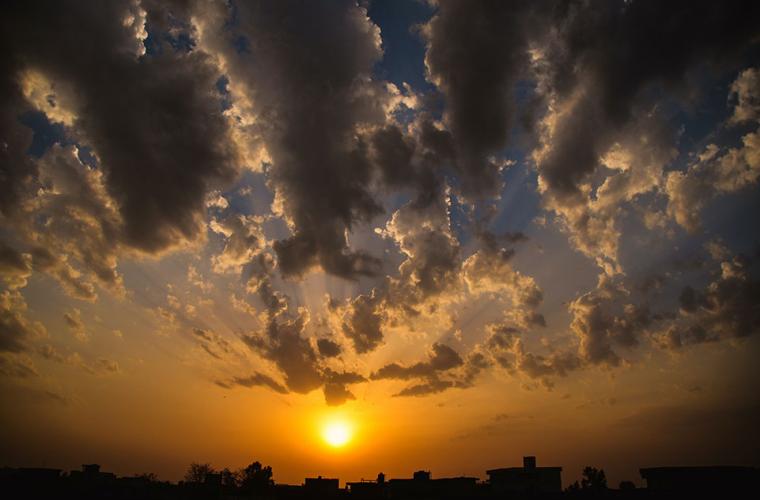 Evening skyline of dark clouds and an orange sun over the rooves of houses