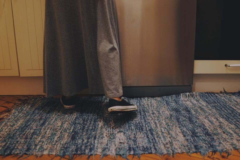 photo of woman's feet on a blue rug by a silver fridge 